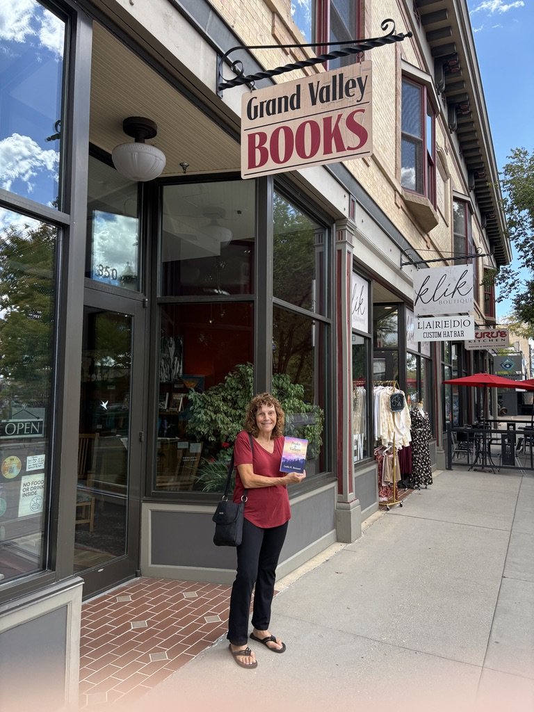 Leslie holding Peaks & Valleys under the Grand Valley Books sign